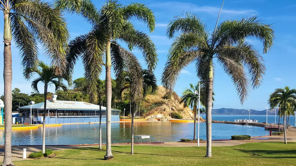 The Rockpool at the northern end of The Strand in Townsville, with palm trees, Kissing Point rising behind the pool and Magnetic Island across the water